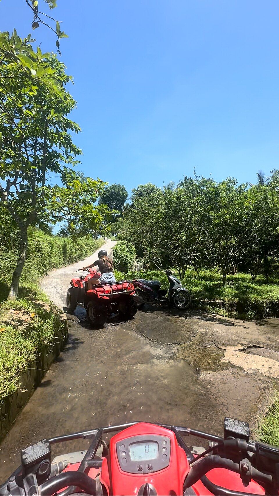 The view from the seat of a quad bike on a muddy farm track in Bali, another rider ahead